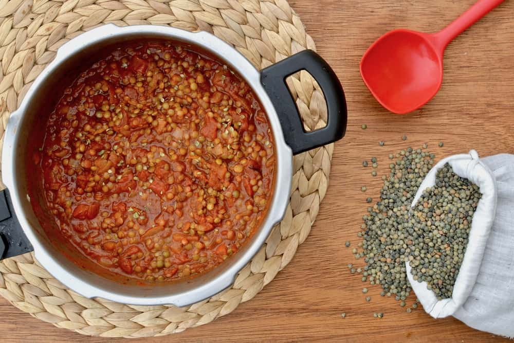 A pressure cooker full of delicious vegan ragu next to a bag of spilt green lentils