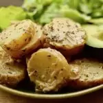Slices of new potatoes in a herby, mustard dressing next to a green salad