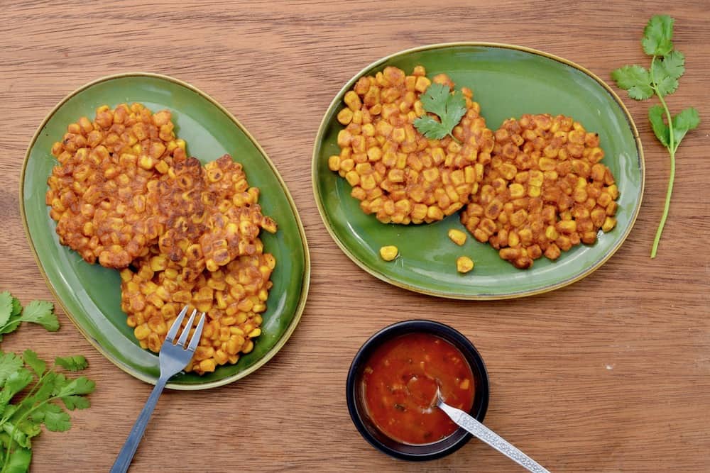 Golden brown sweetcorn fritters with a side of sauce and coriander