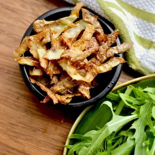A small dish of crispy, golden brown crisps next to a plate of rocket