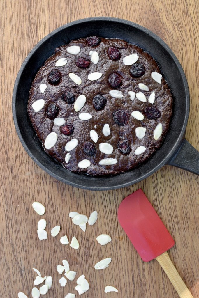 A brownie dough covered in almonds and cranberries in a cast iron skillet