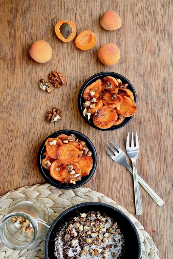 Grilled apricot and walnut dessert surrounded by fresh apricots and a jar of walnuts