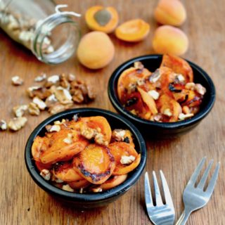 Two dishes of grilled fresh apricots topped with walnuts