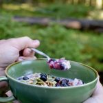 Taking a spoonful of blueberry porridge in the woods
