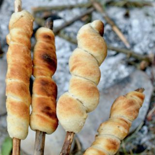 Four sticks wrapped in crusty bread in front of a campfire