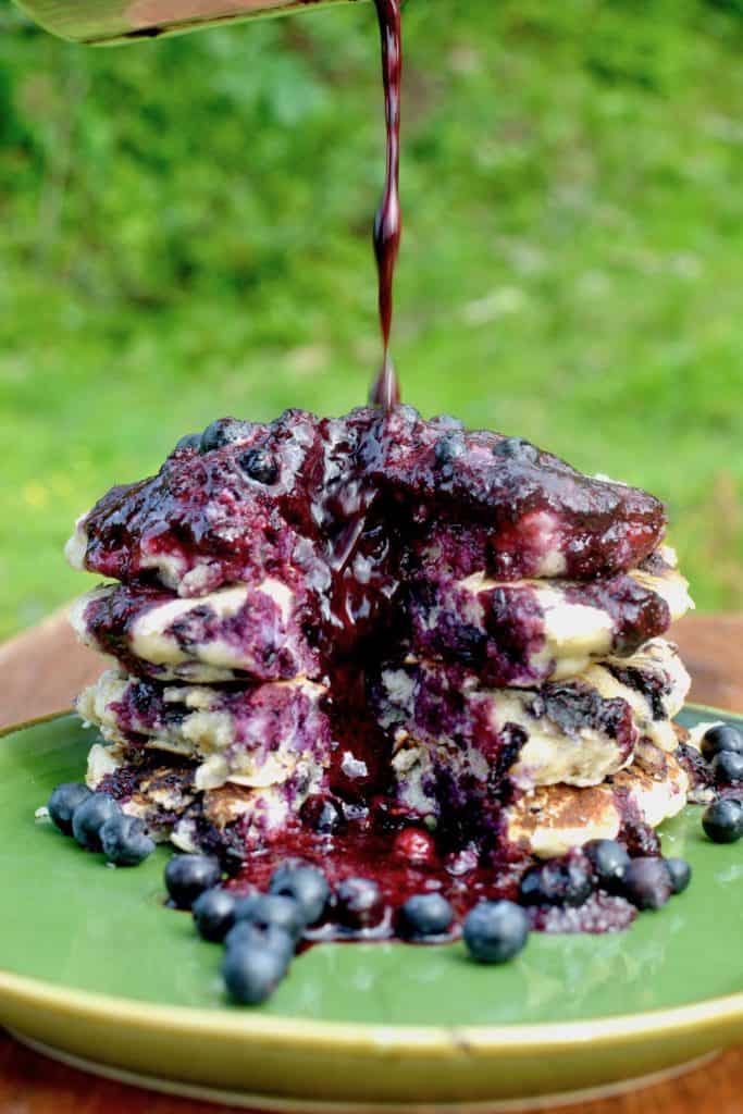 A stack of mouthwatewring blueberry pancakes with a stream of berry sauce 
