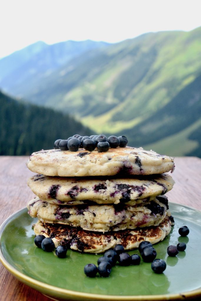 A stack of wholesome vegan blueberry oat pancakes with mountainsin the background
