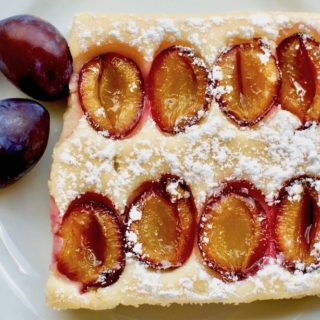 A piece of light vegan sponge cake with plums and icing sugar on top.