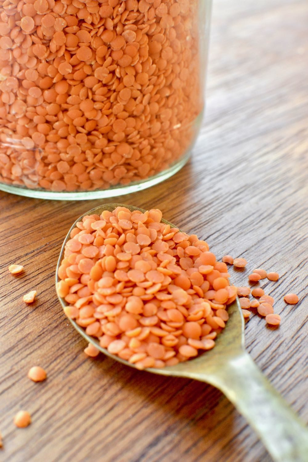 Red lentils on a spoon showing their pinkish orange colour and disc shape