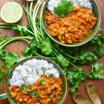 Two green bowls filled with red lentil dal, white rice and garnished with coriander leaves