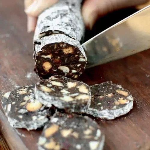 A knife cuts into a chocolate salami filled with biscuits and nuts