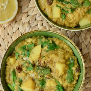 Yellow coloured dahl with chunks of potato and wilted green spinach in a green bowl