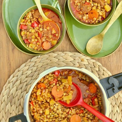 A pressure cooker full of lentil stew with a red ladle, and two bowls of stew ready to eat