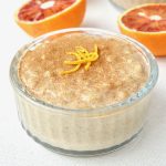 A glass ramekin of rice pudding, topped with cinnamon and orange zest