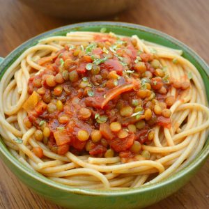 Lentils in a rich red tomato sauce on top of a bowl of spaghetti