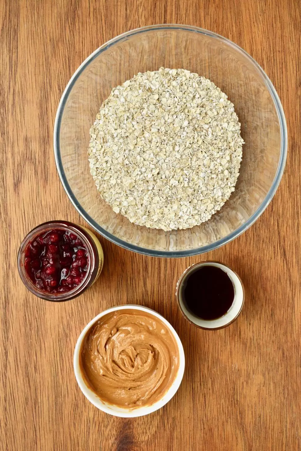 Ingredients on a wooden board - a bowl of oats, jar of jam, maple syrup and smooth peanut butter