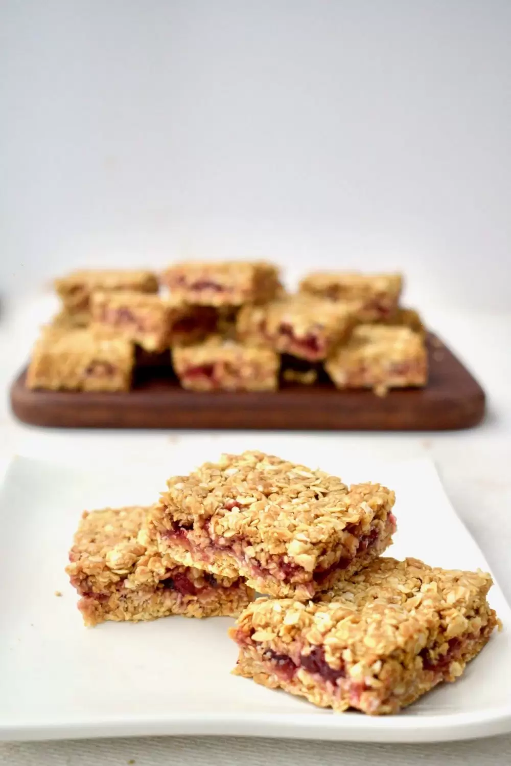 Three vegan oat bars on a plate, with the remaining bars in the background