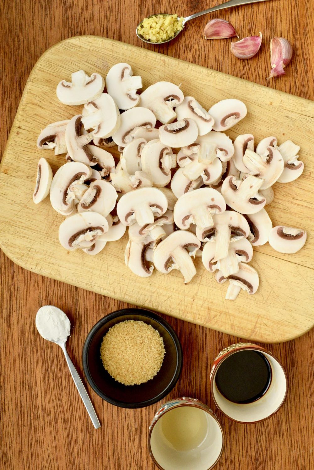 Sliced white mushrooms on a board next to ingredients for teriyaki sauce