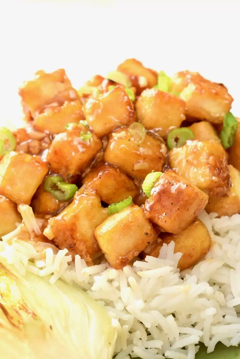 A sticky, shiny lemony sauce covering cubes of tofu on top of white rice.