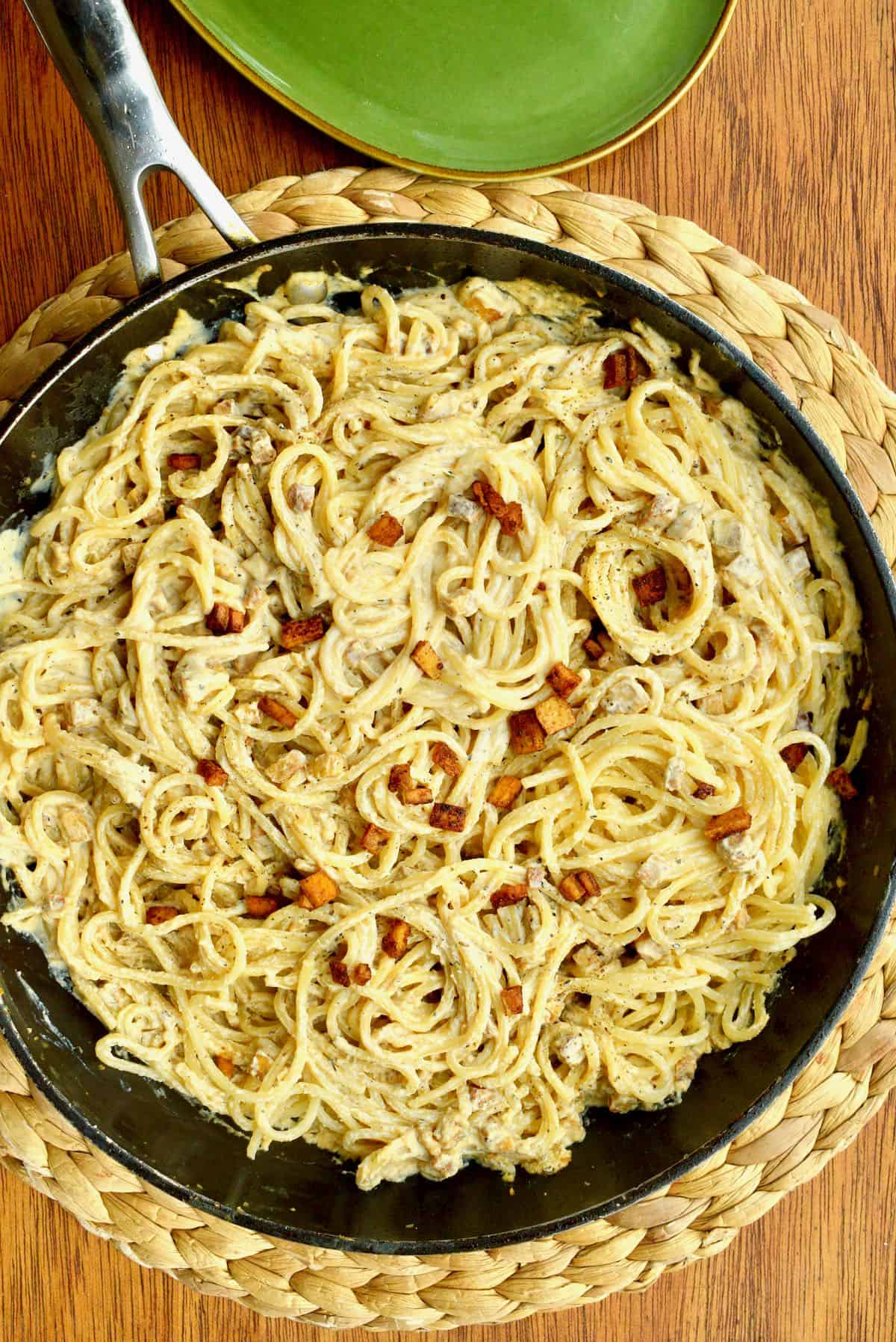 A large frying pan full of spaghetti in a creamy sauce and tofu bits. 