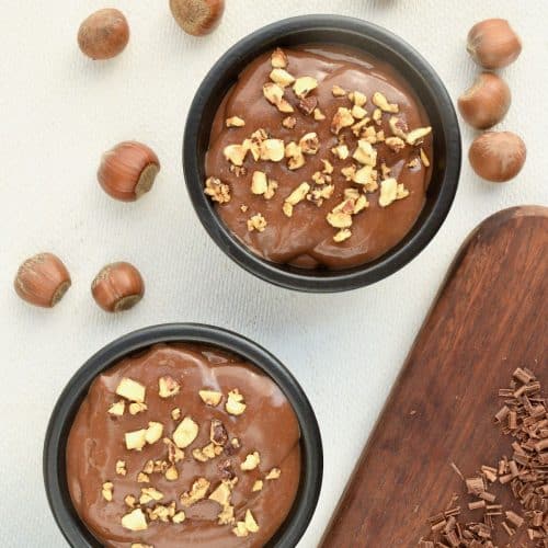 Two dishes of smooth chocolate pudding topped with crispy nuts