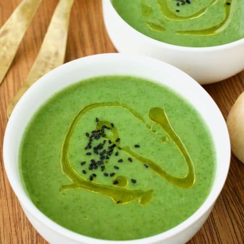 Two white bowls of green nettle soup. A swirl of olive oil and black nigella seeds on top.