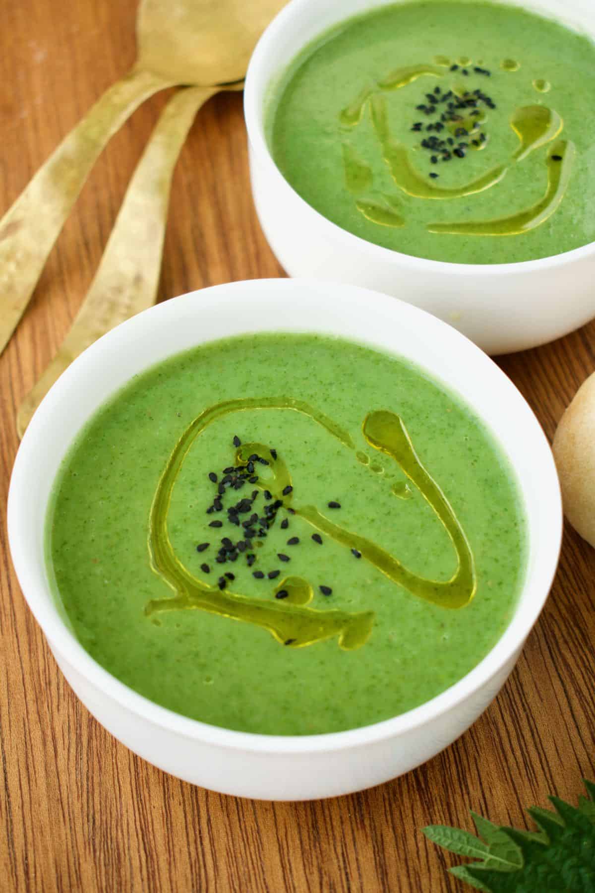 Two white bowls containing bright green nettle soup.