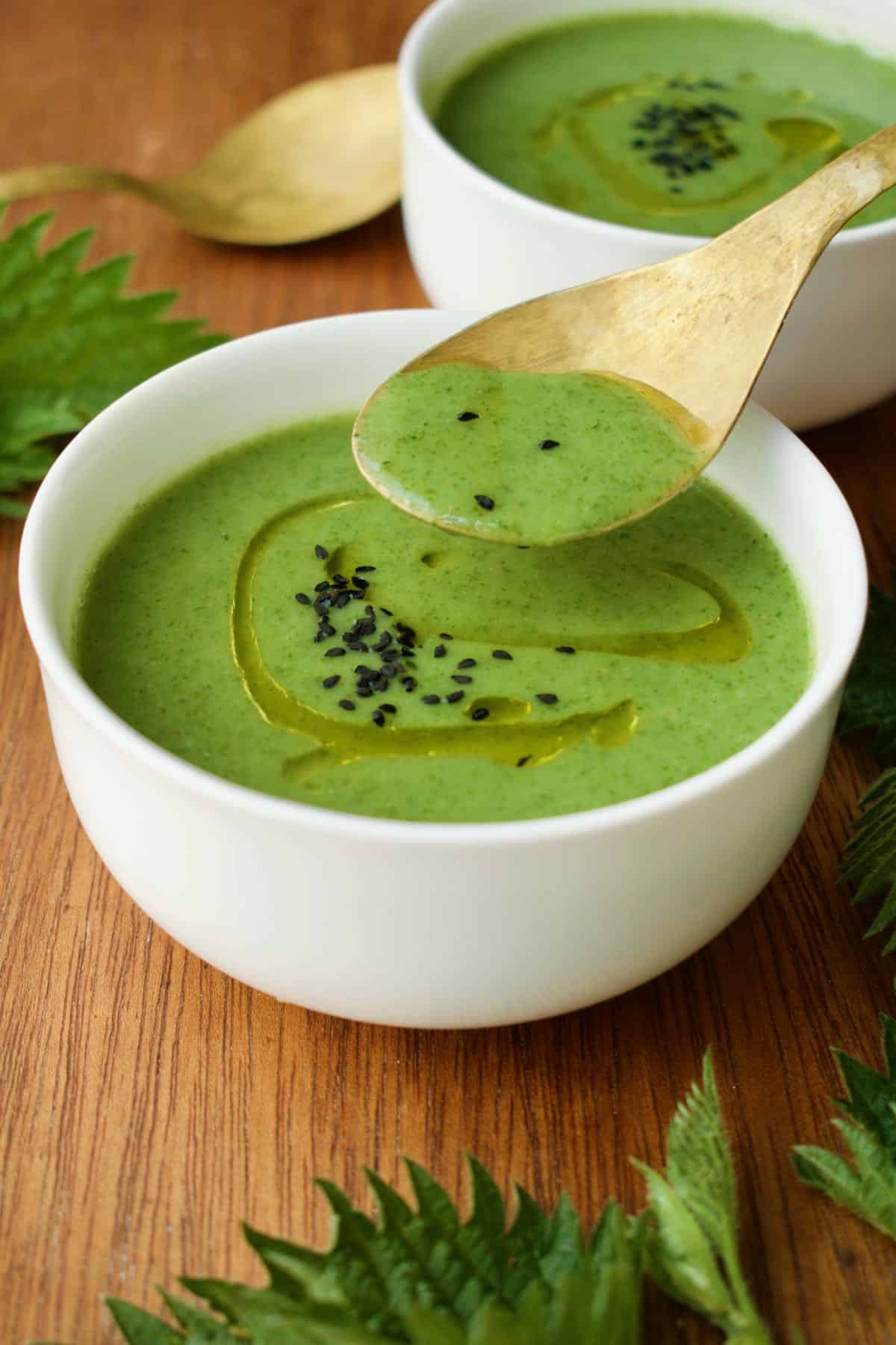A golden spoon scoops a spoonful of the vibrant and fresh looking nettle soup.