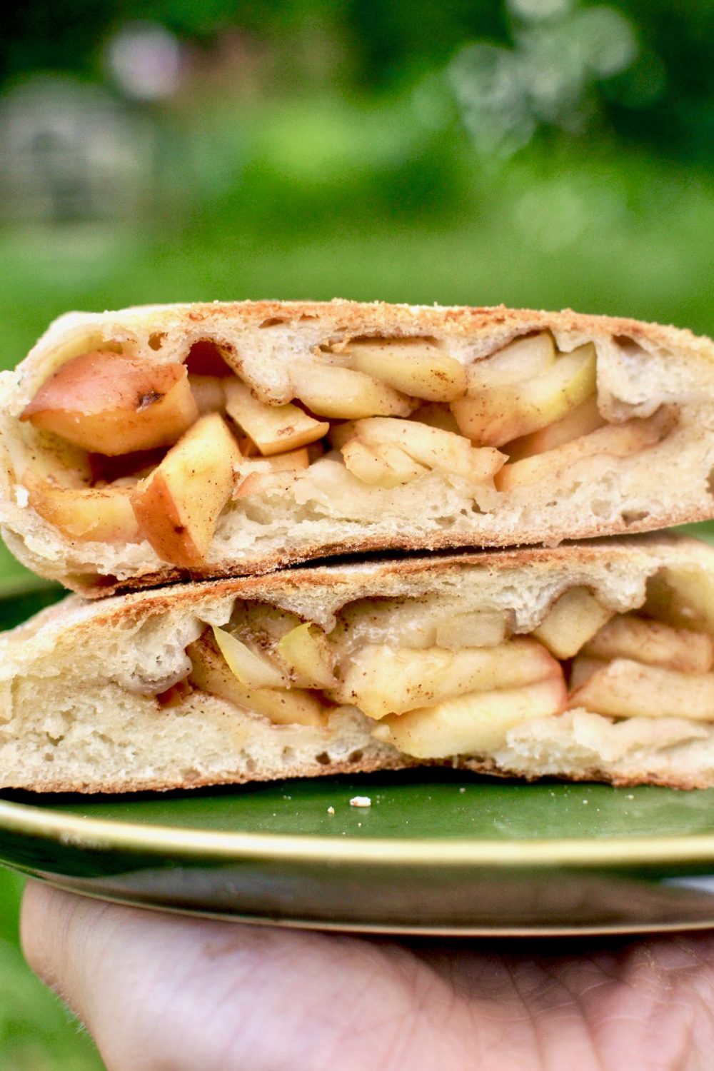 An applestrudel flavoured calzone. Its two halves are stacked on a plate, revealing the filling of apple and a sprinkle of cinnamon.