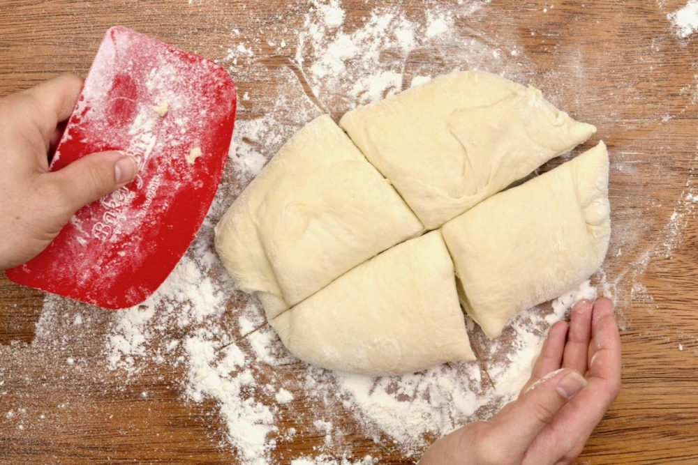 The pizza dough is tipped onto a floured wooden surface and split into four even portions.