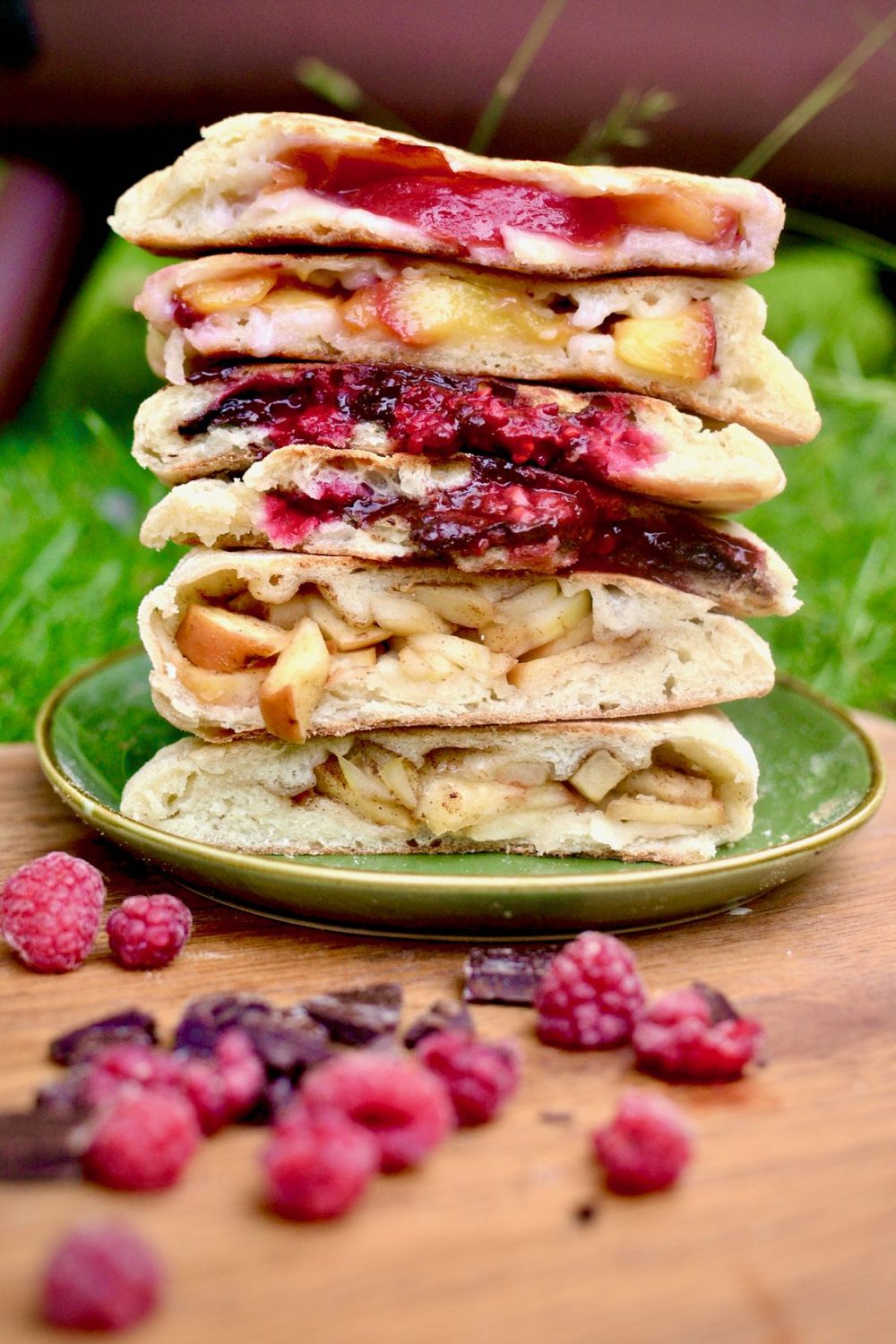 Different filled sweet pizzas cut in half and stacked on top of each other: There are fillings of peach and coconut cream, raspberry and chocolate, and apple and cinnamon.