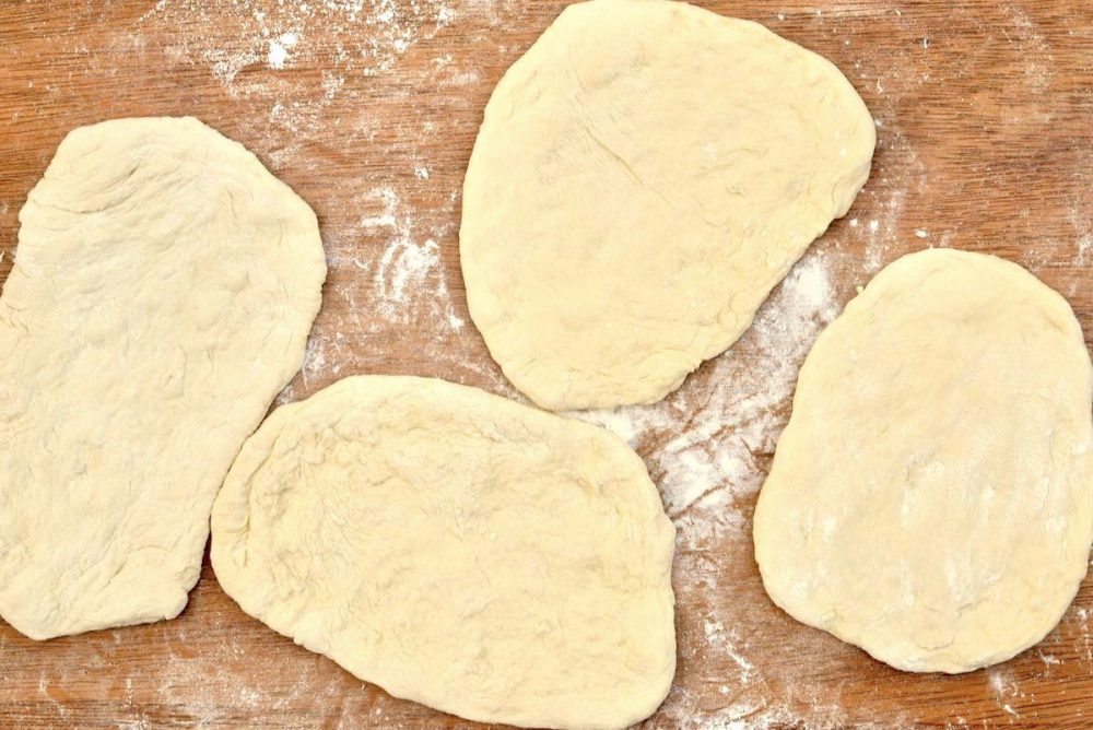 The four portions of dough have been shaped into flat ovals to form the bases for the filled pizzas.