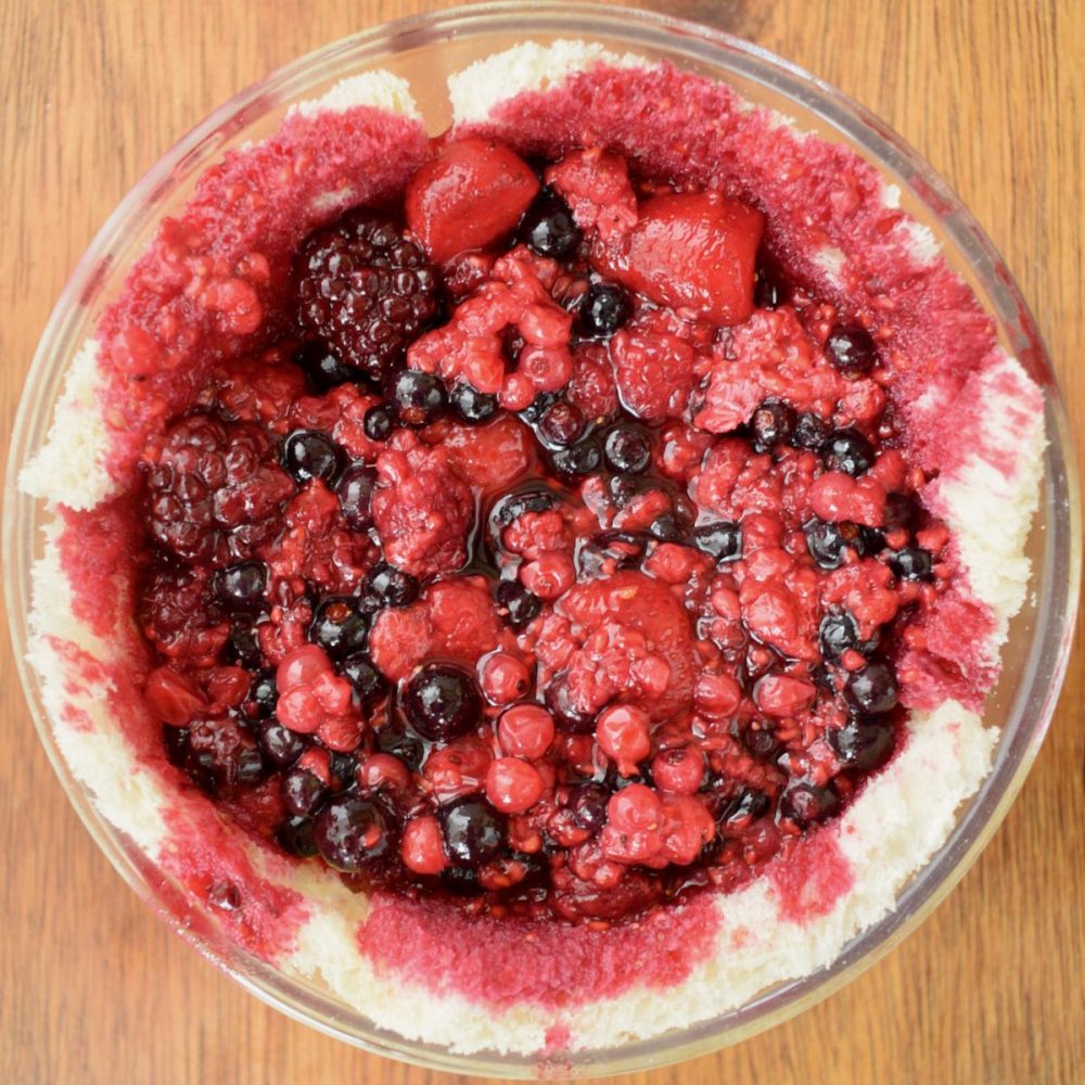 The cooked red berries are now filling the bowl that was previously lined with white bread. The bread is starting to soak up the red berry juice.