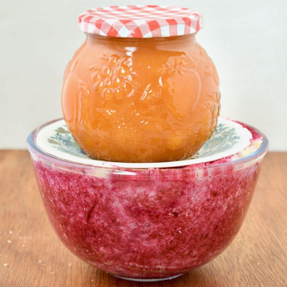 A jar of orange coloured apricot jam is placed as a weight on a plate on top of the pudding. The process is compacting the pudding and helps the bread soak up the red berry juice.