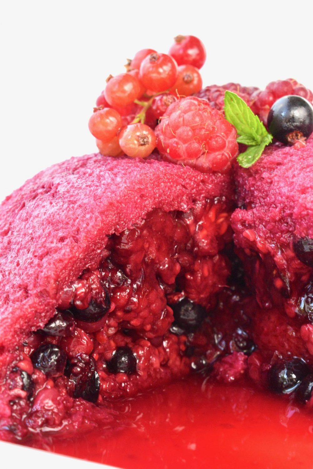 A close up view of the revealed inside of the pudding. The red and dark purple berries are tightly packed under a slice of bread red with soaked up juice.