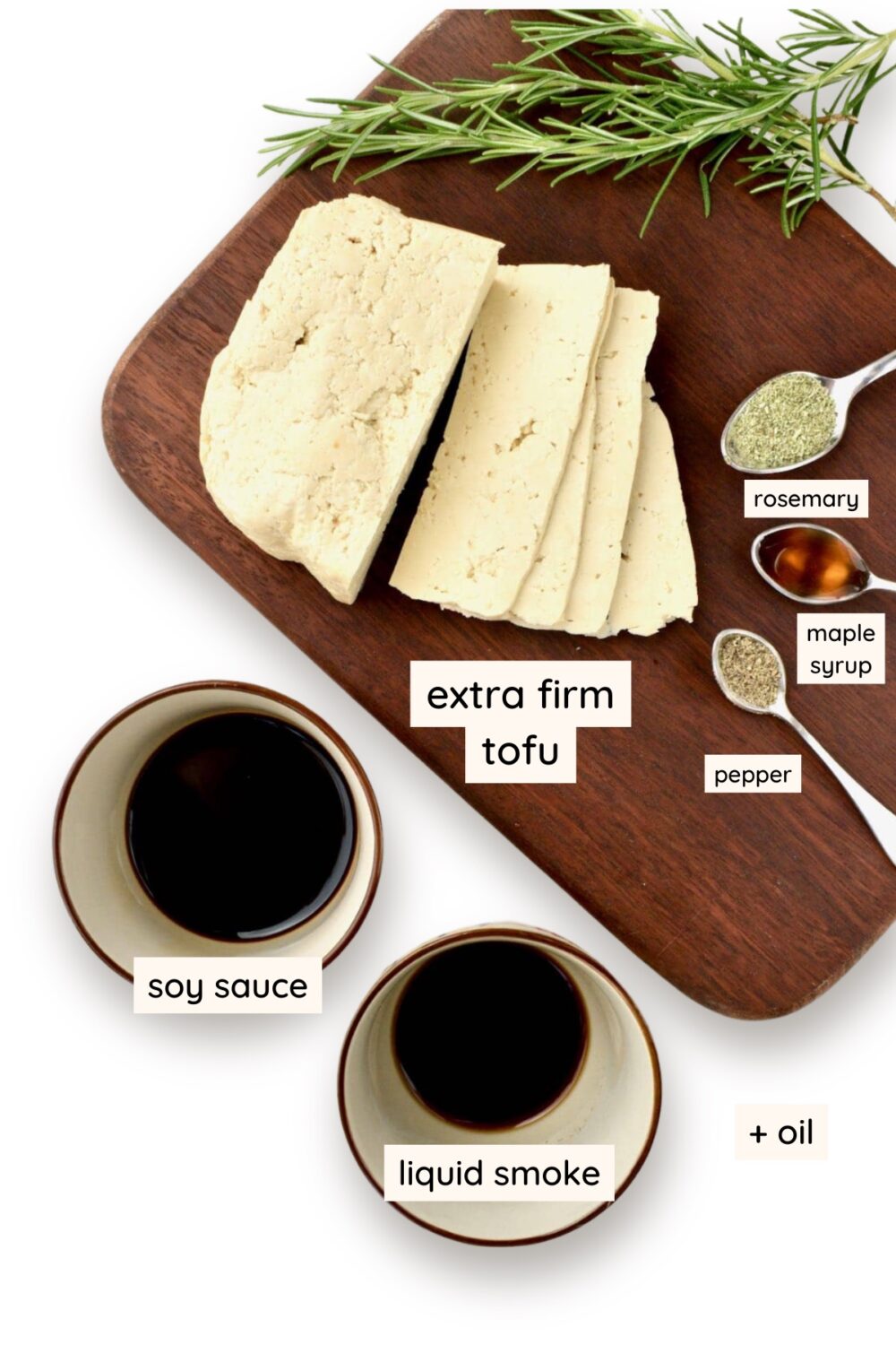 Tofu slices on a dark wooden board, ground rosemary, maple syrup and black pepper on small measuring spoons, and soy sauce and liquid smoke in small pots.