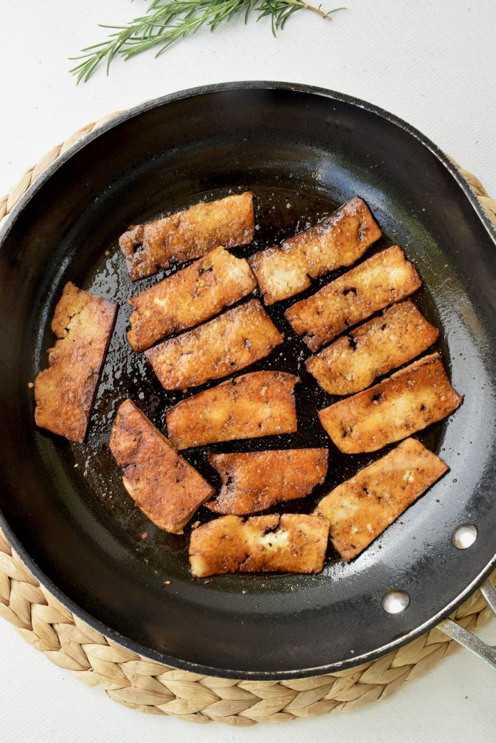 Slices of brown fried tofu in a large frying pan.