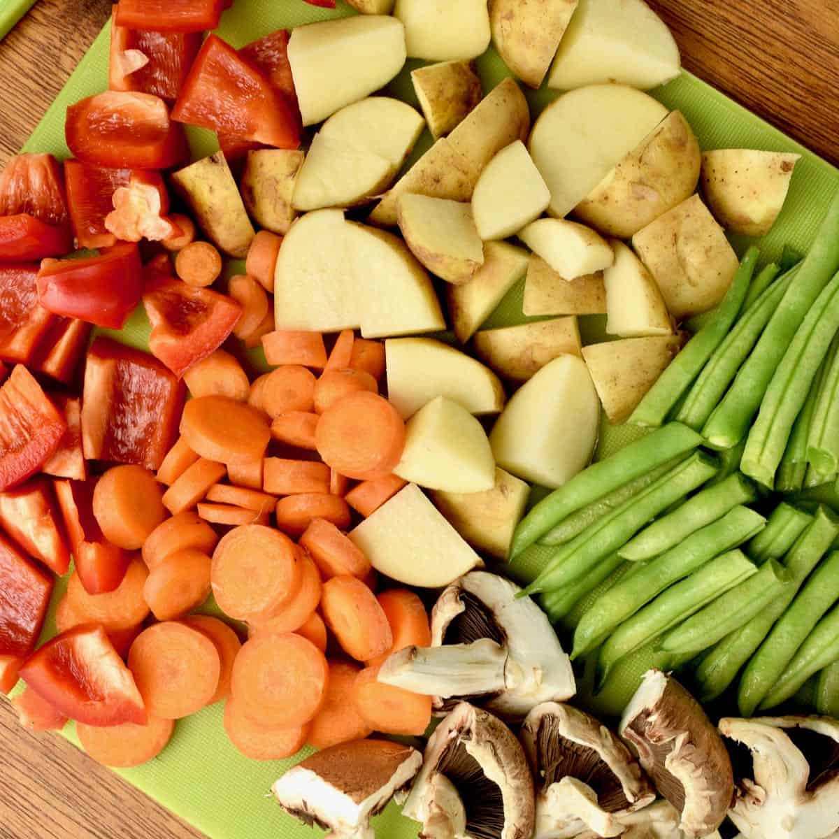 Diced potatoes, red pepper, mushrooms, slice carrots and green beans on a chopping board.