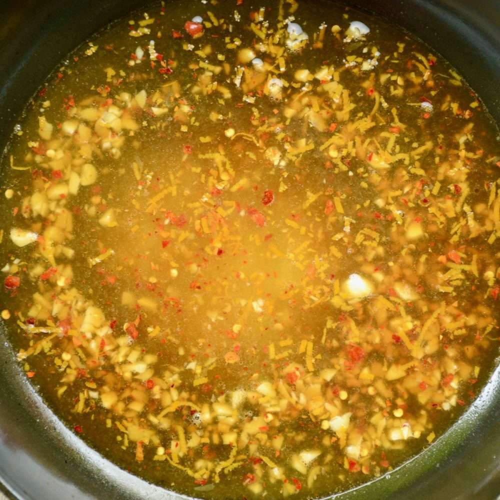 A vibrant orange sauce. Bits of lemon zest, garlic and ginger flakes are visible.