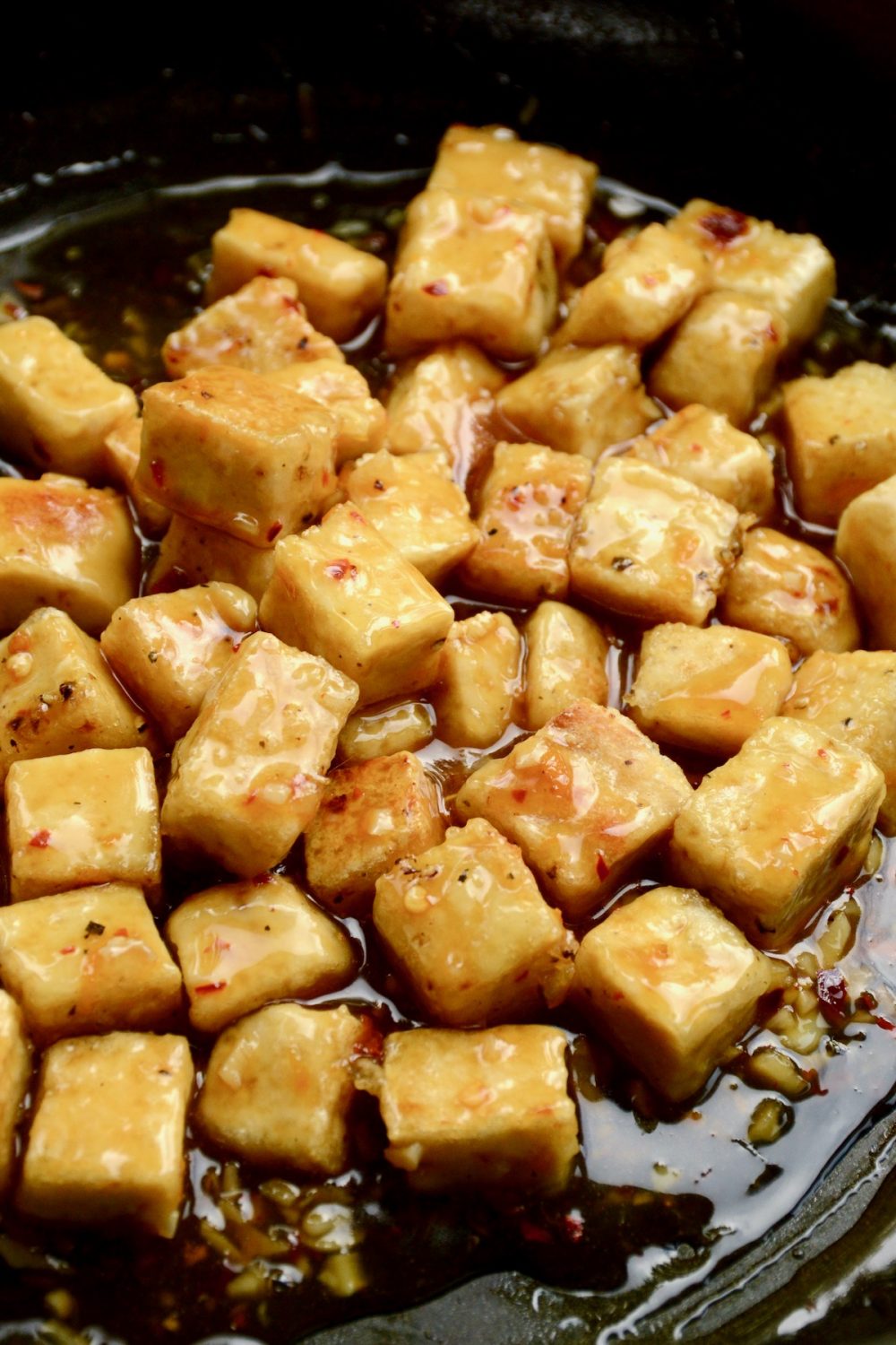 The fried tofu cubes have been added back into the pan and coated in the orange sauce.