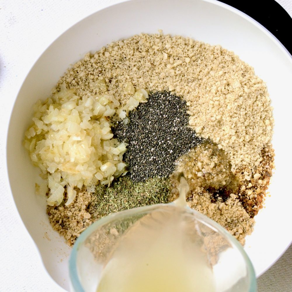 All the ingredients for the burger mix are combined in a mixing bowl: Ground nuts, bread crumbs, sauteed onion, dried herbs, chia seeds, soy sauce and vegetable bouillon.