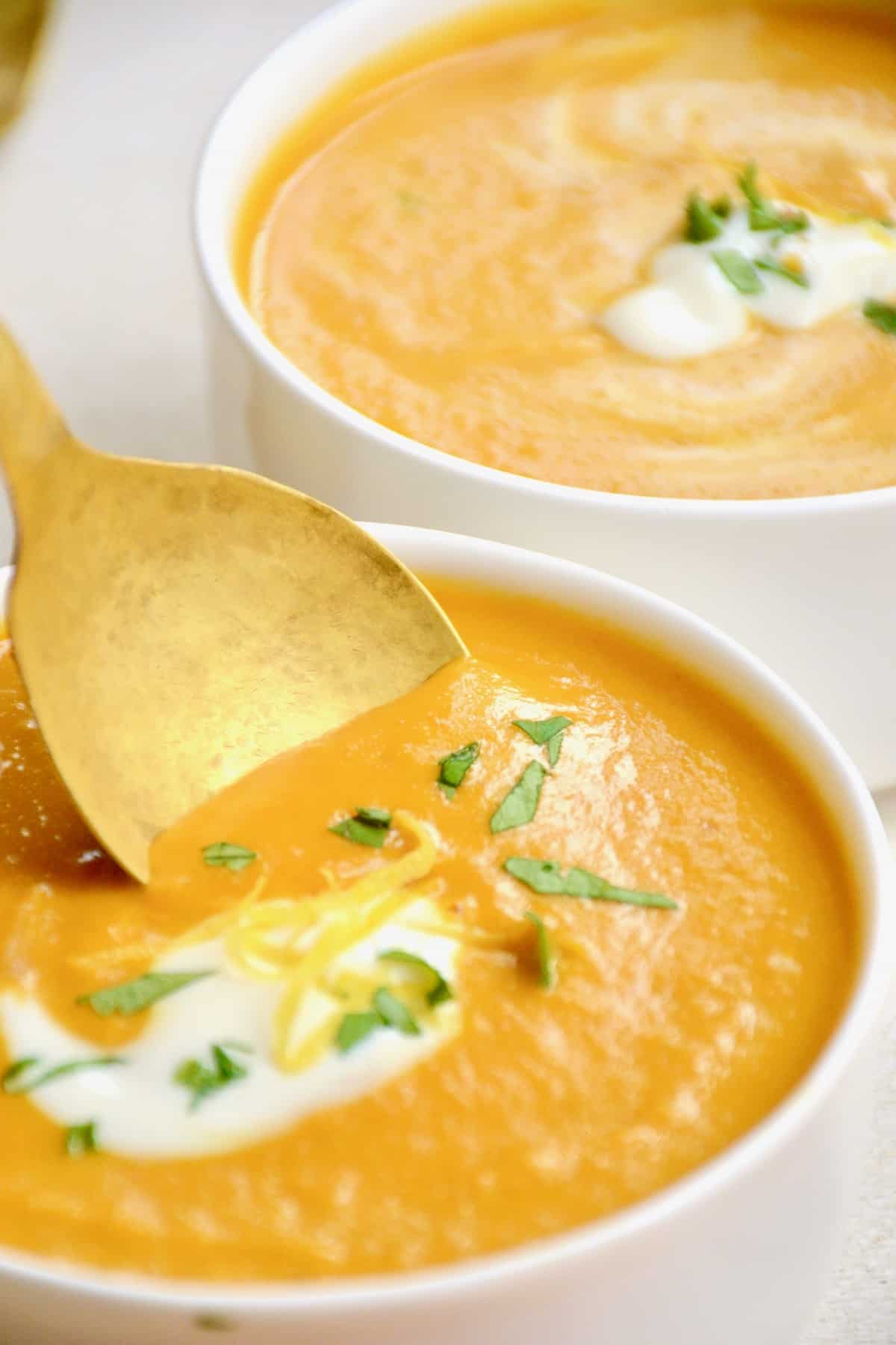 Dipping a spoon into the thick, orange coloured soup.