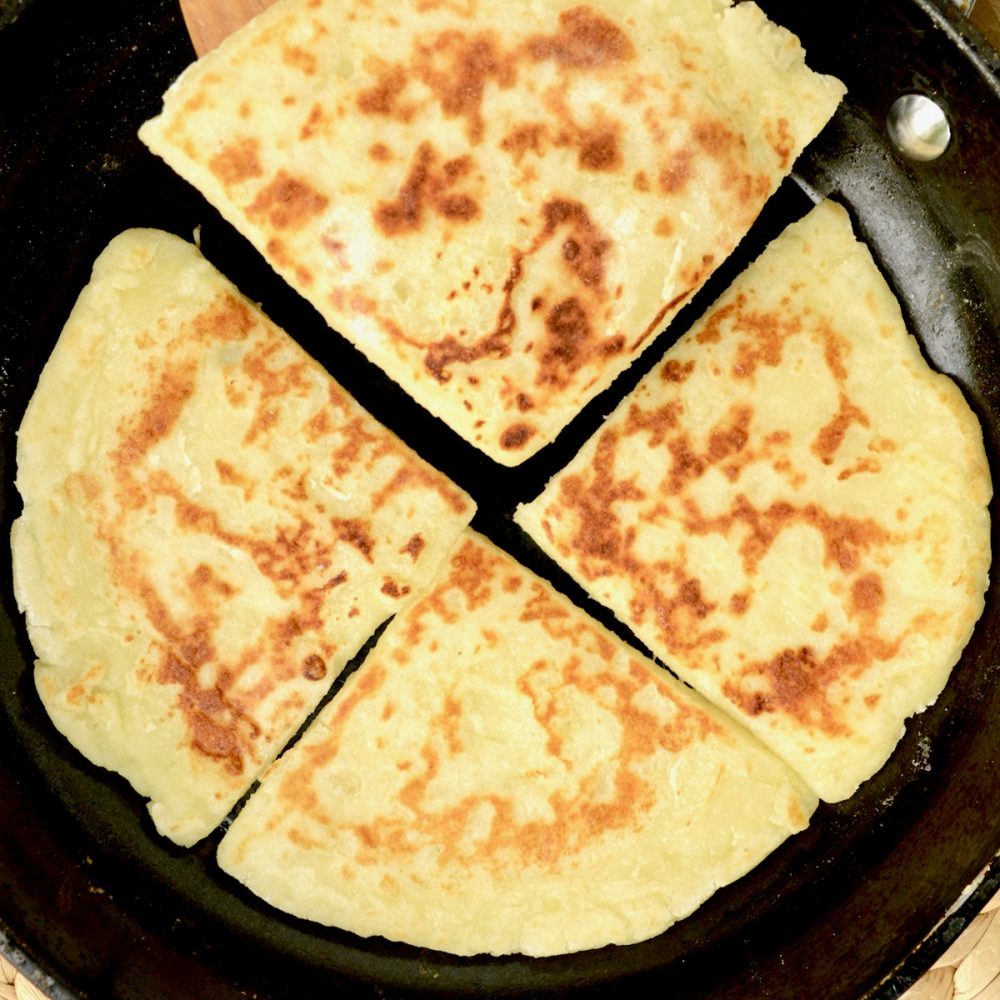 Four cooked tatty scones in a frying pan. Their surface is sprinkled with brown, crusty parts.