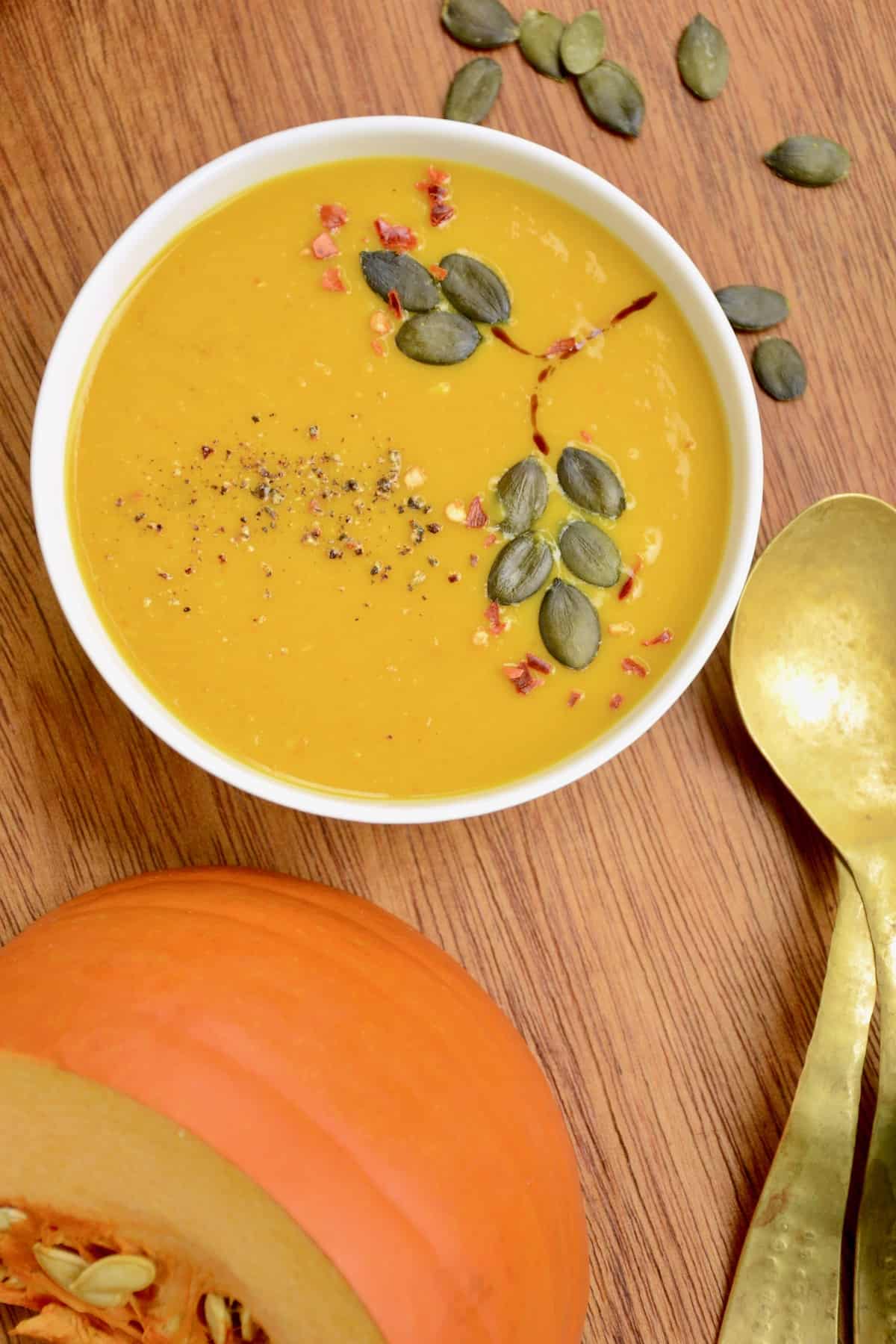 A bowl of soup next to a wedge of pumpkin.