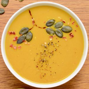 The pumpkin soup is garnished with pumpkin seeds and chili flakes in an autumnal tree pattern.