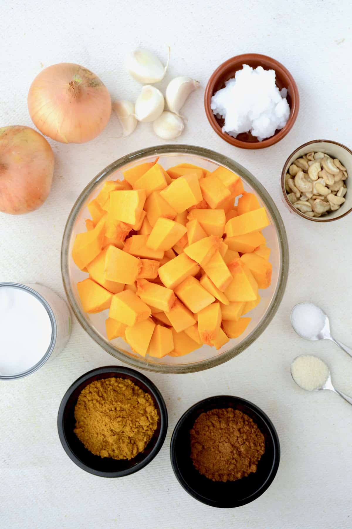 A bowl of pumpkin cubes, spices, onion, garlic, cashews, coconut oil and coconut milk on a white board.