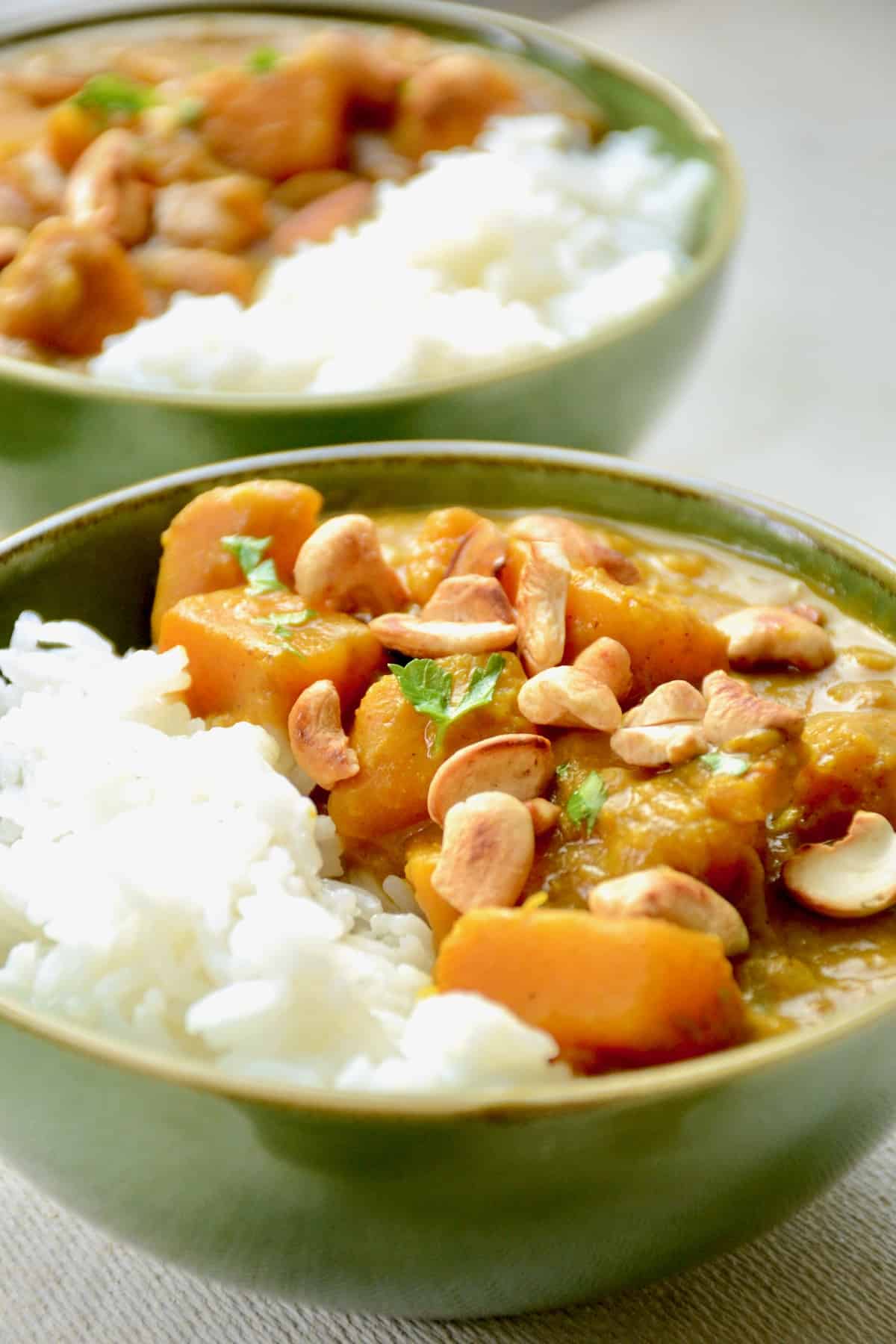 Two bowl of pumpkin curry with golden toasted cashews and sprinkling of herbs on top.