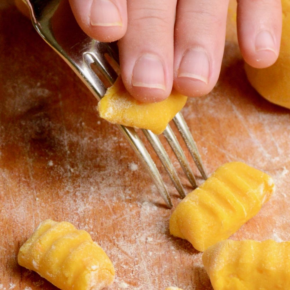 Rolling a piece of dough over the back of a fork to form a ridged gnocchi shape.