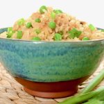 A blue green pottery bowl filled with a heap of vegan fried rice.