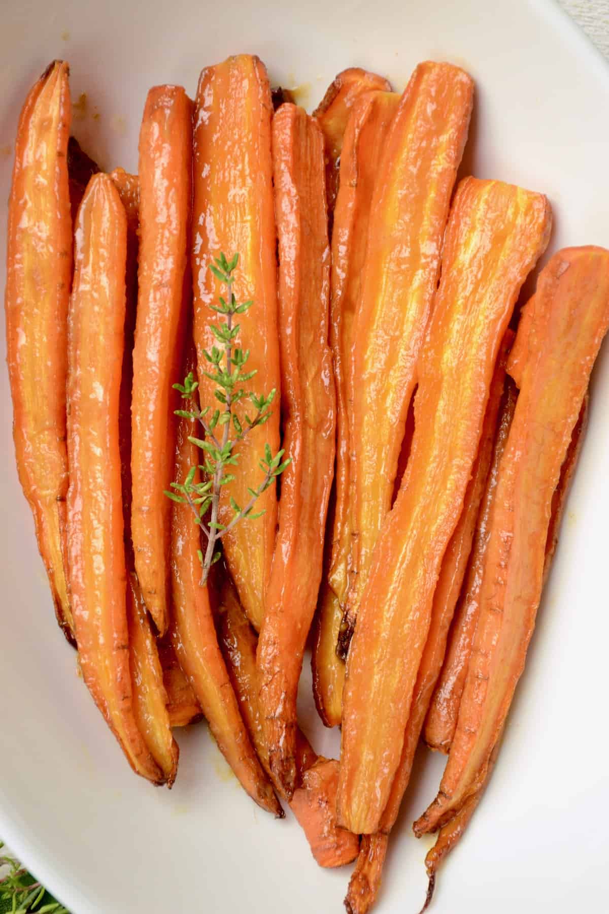 Glazed carrots in a serving dish with a twig of fresh thyme.